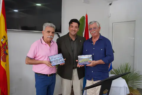 Tres asistentes posan en el acto institucional mientras dos de ellos muestran placas conmemorativas.