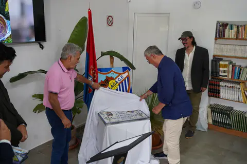 Dos asistentes retiran una tela blanca para mostrar el rótulo cerámico Afición Malaguista.