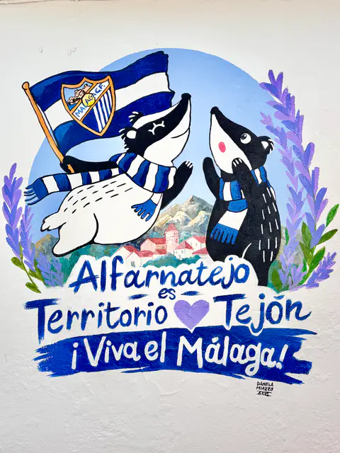 Mural de Alfar y Natejo con bufandas y una bandera blanquiazul sobre el paisaje de Alfarnatejo.