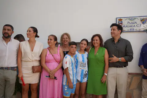 Parte del grupo de asistentes posa junto a jóvenes con camisetas blanquiazules y el rótulo de la plaza.