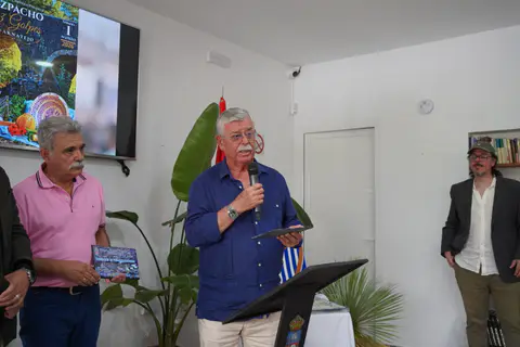Un asistente interviene con un micrófono y una placa ante el público del acto institucional.