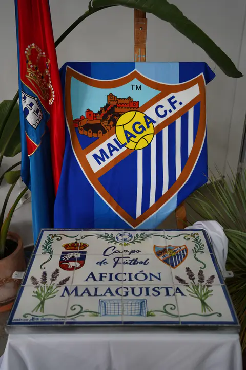 Escudo blanquiazul y rótulo cerámico del campo de fútbol Afición Malaguista en composición vertical.