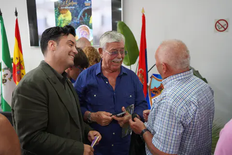 Tres asistentes conversan durante la jornada con banderas y un escudo blanquiazul al fondo.