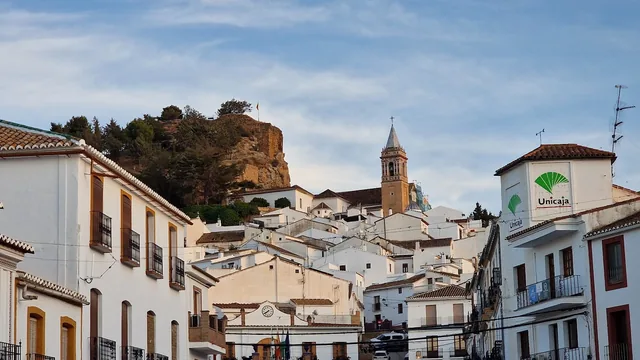 Vista de una calle de Ardales con casas blancas, iglesia y peña al fondo.
