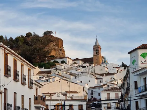 Vista de una calle de Ardales con casas blancas, iglesia y peña al fondo.