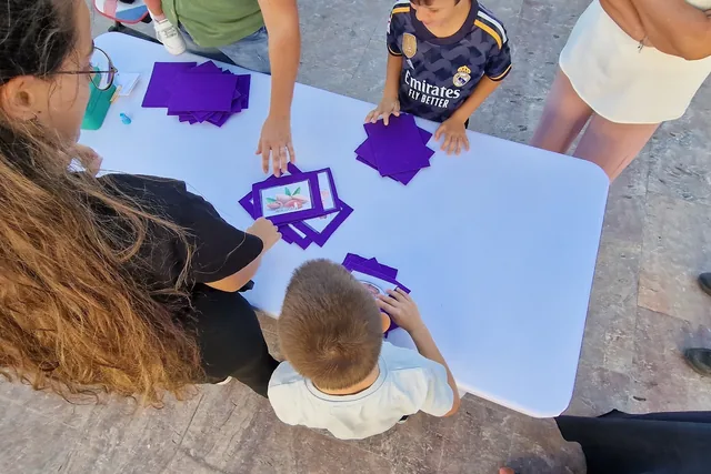 Manos colocando recortes morados sobre una mesa de trabajo.