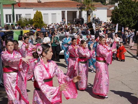 Desfile en una calle blanca con participantes vestidos en tonos rosas.
