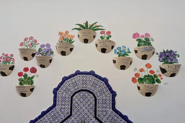 Mural cerámico de macetas y flores alrededor de una fuente.