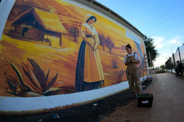 Persona junto a un gran mural de temática rural.