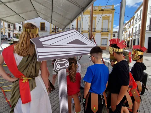 Figuras de ambientación romana recorriendo una calle con familias.