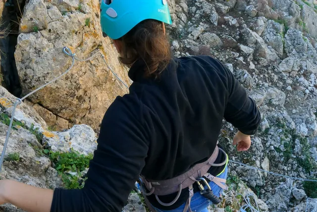 Persona con casco descendiendo por una pared rocosa.